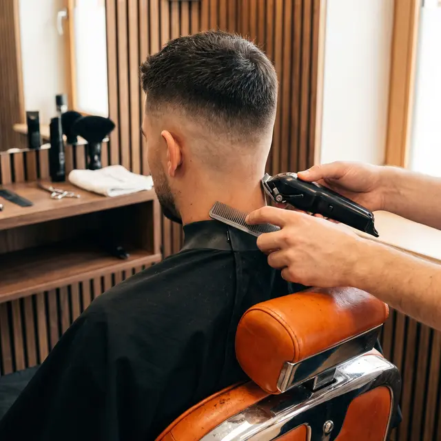 Kurzer Herrenschnitt mit Fade im Nacken, eine Hand führt die Haarschneidemaschine